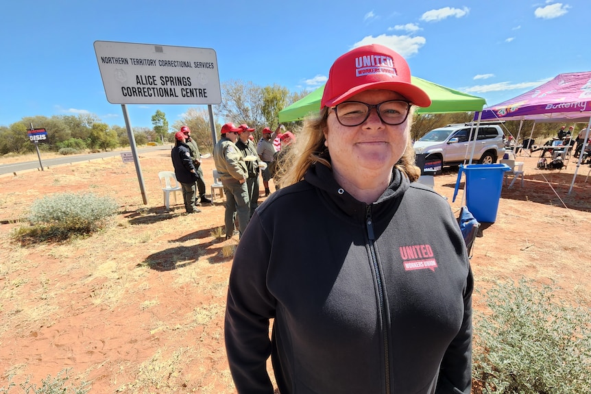 A woman wearing union logos stands before a small crowd in a desert town