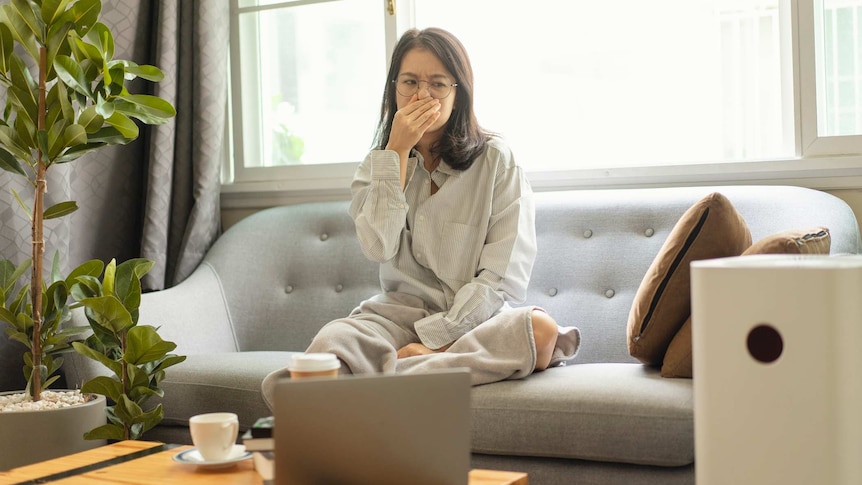 Woman on couch holding her nose looking at an air purifier