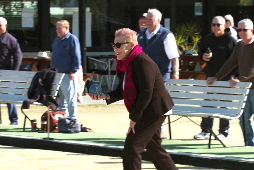 A woman plays bowls as a large crowd watches on