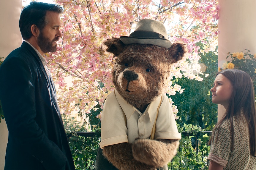 A man, a tall bear wearing a hat, and a young girl.