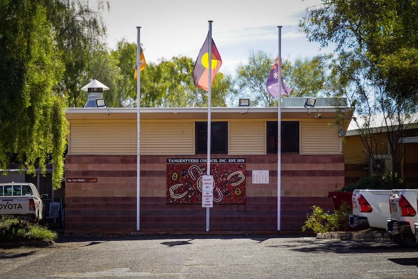 A photo of a simple Tangentyere Council building, with three flags flying out the front.