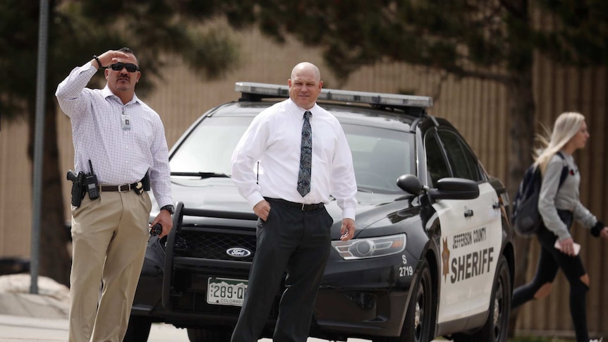 Columbine High School principal Scott Christy (right) joins an officer in watching as students leave the school.