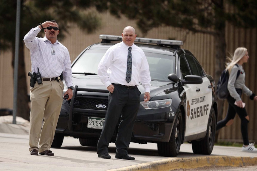 Columbine High School principal Scott Christy (right) joins an officer in watching as students leave the school.