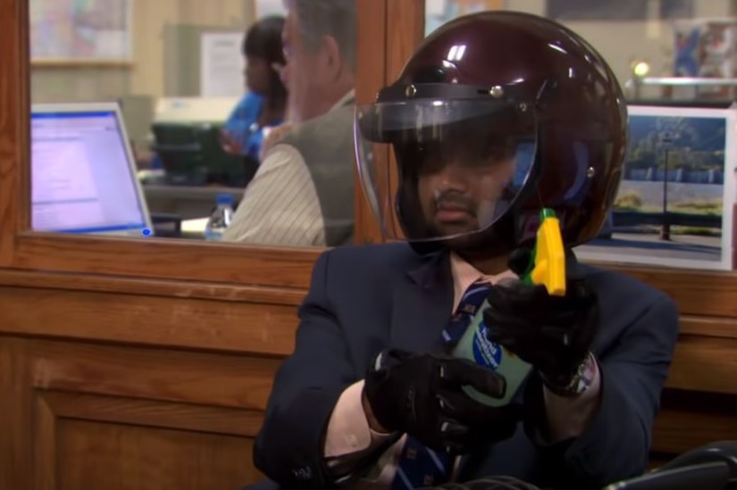 Tom Haverford wears a suit with a motorbike helmet and holds hand sanitiser in a spray bottle