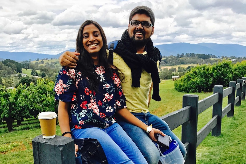 A couple sit on a fence in the country