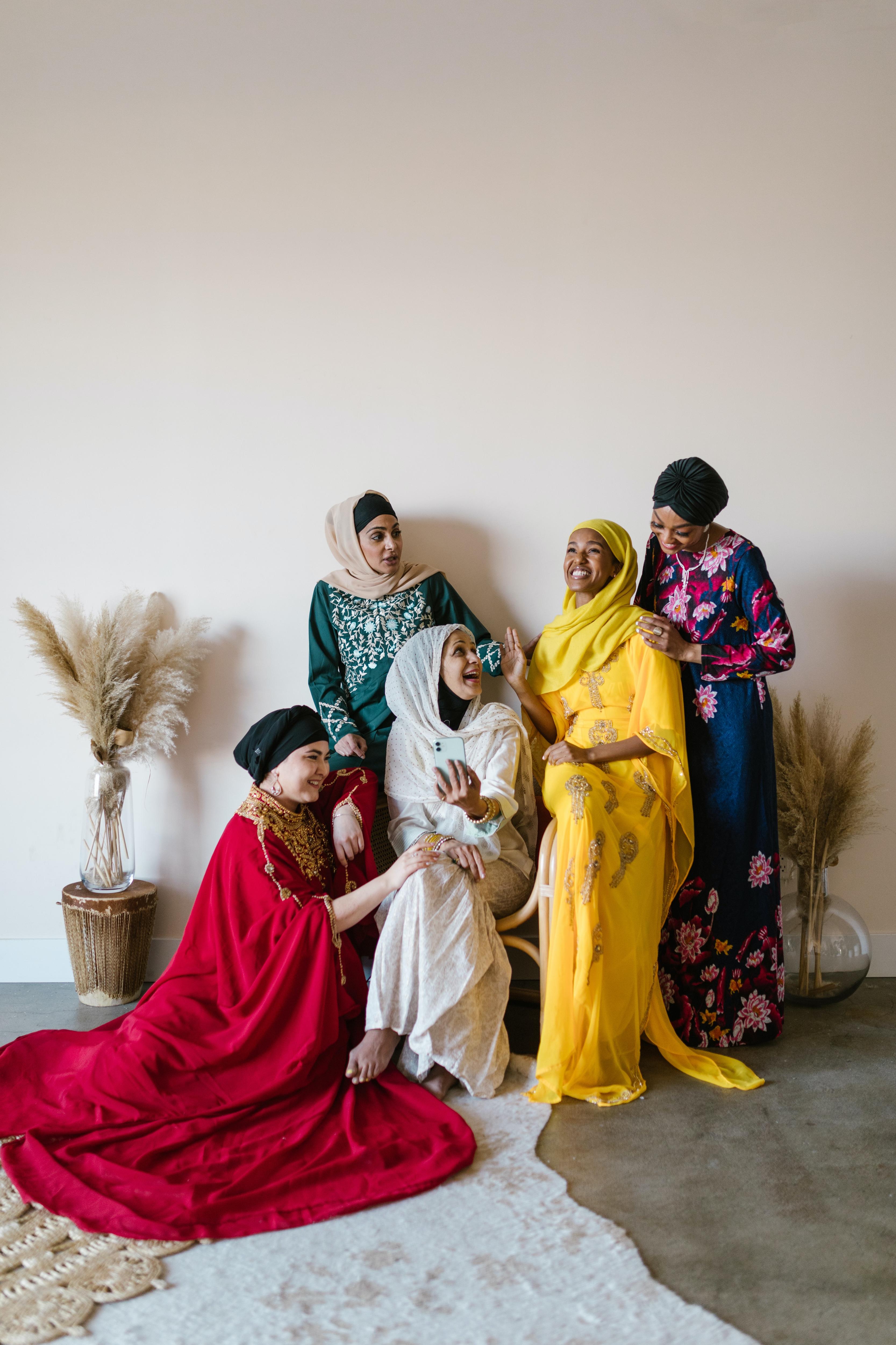 Five women in colourful dresses sitting together and laughing.