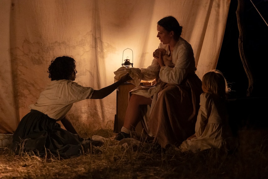 Scene from the movie of a mother holding her newborn baby as her daughter and young Aboriginal woman look on