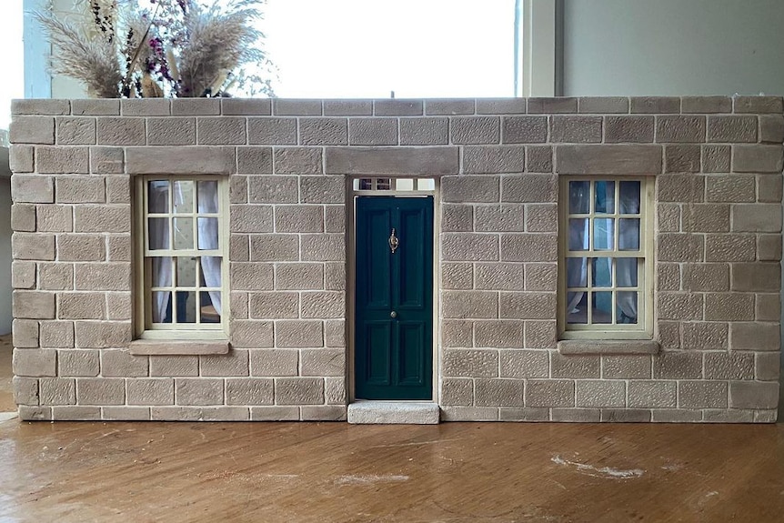 Photograph of a miniature sandstone cottage front with no roof.