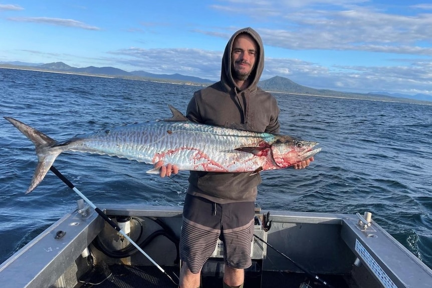 Luke standing in his boat holding a large mackerel fish. 