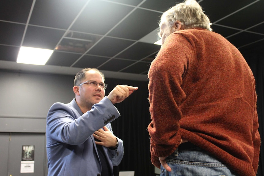 Jamie on stage giving directions and pointing at another actor during a rehearsal.