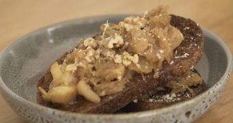 Braised fennel on rye toast with crushed walnuts and Padano cheese, two slices sit in a blue bowl on a kitchen bench.