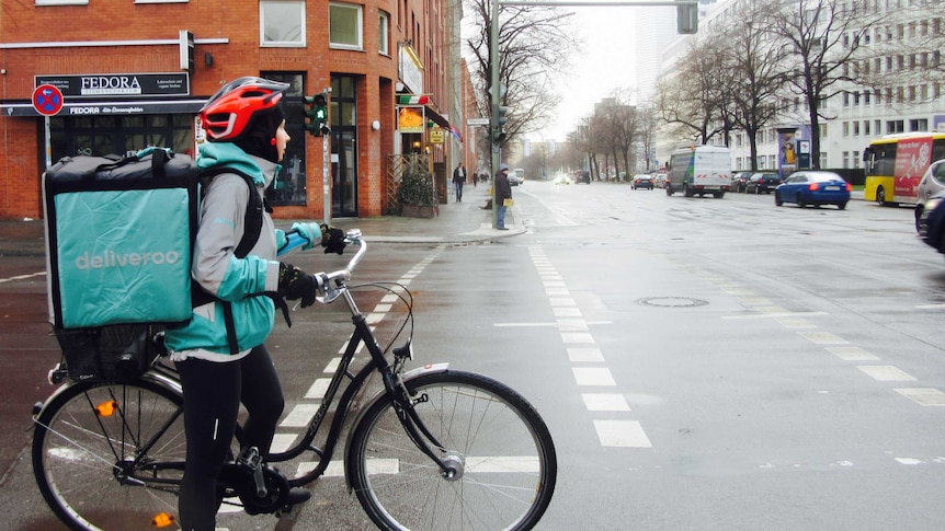 A deliveroo rider waits on a  bike at an intersection.