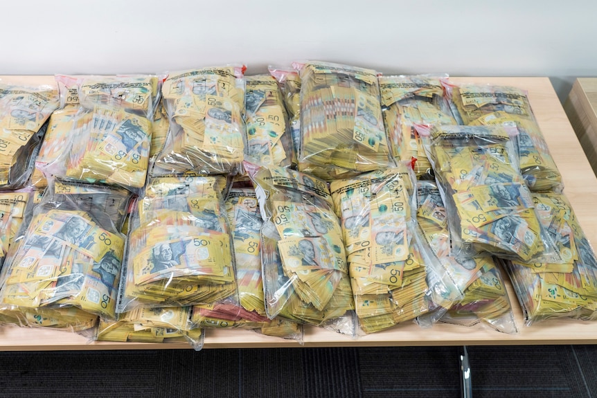 Piles of 50 dollar notes in plastic bags displayed on a table 