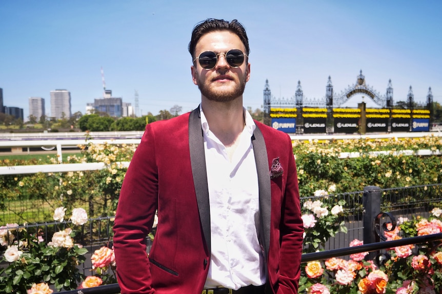 A young man wearing a red suit, white shirt and dark sunglasses.