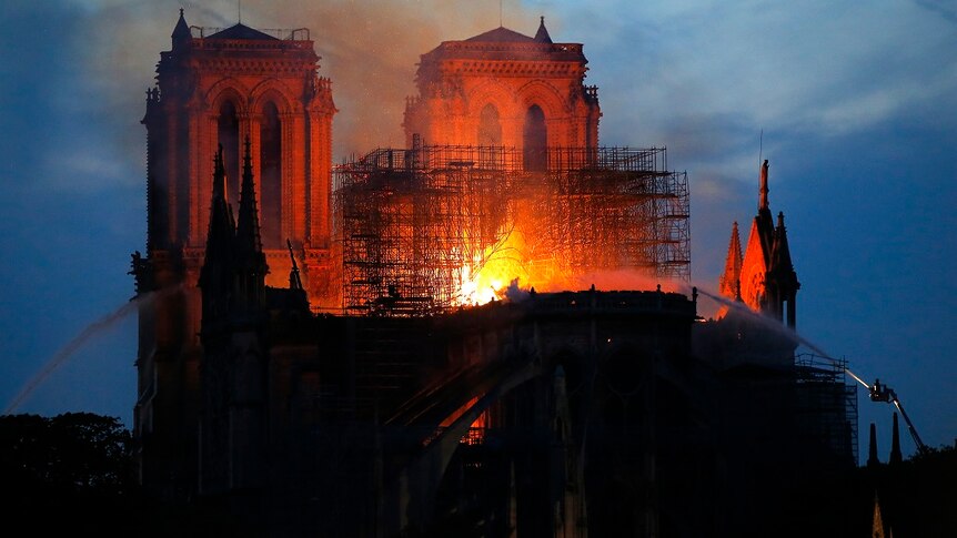 Flames burn through a cathedral while firefighters on raised platforms spray water