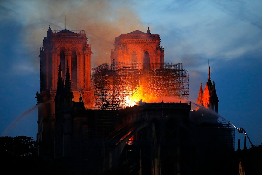 Flames burn through a cathedral while firefighters on raised platforms spray water