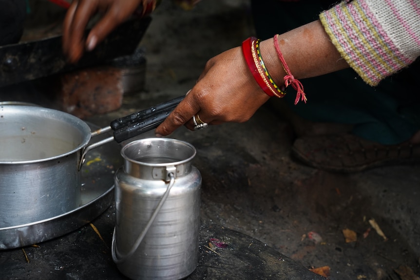 A close-up shows a woman holding a saucepan. She has several bracelets on her wrist