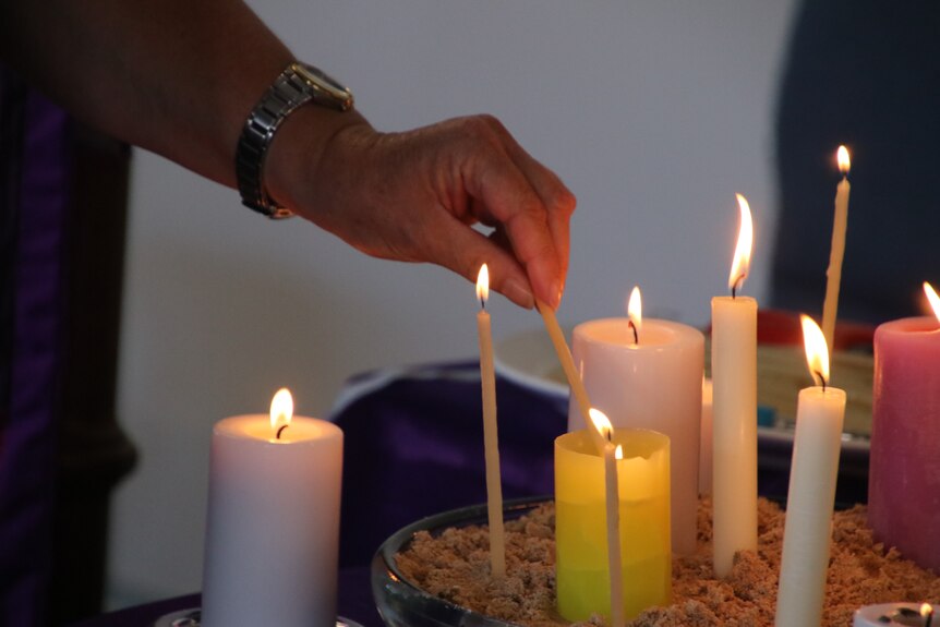 A woman's hands lights several candles on a table