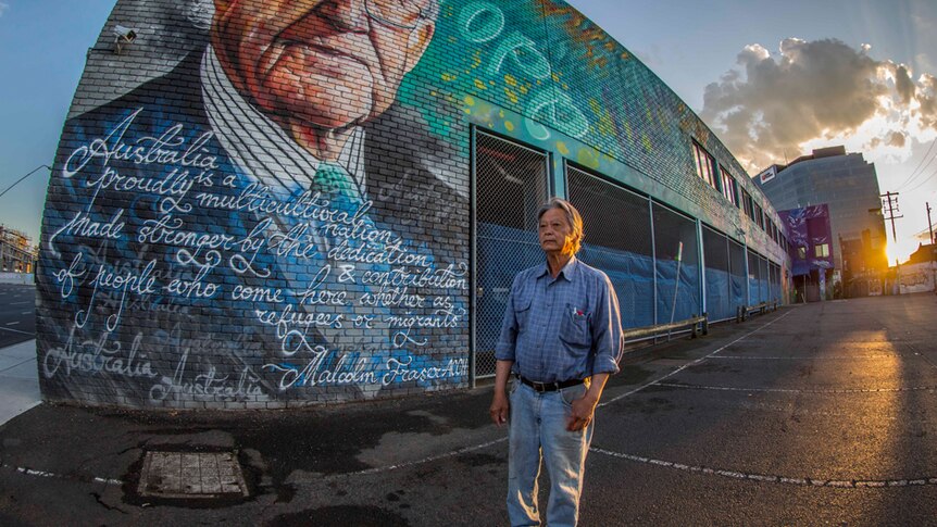 Vietnamese refugee Henry Thompson Huynh stands in front of a street art painting of Malcolm Fraser.