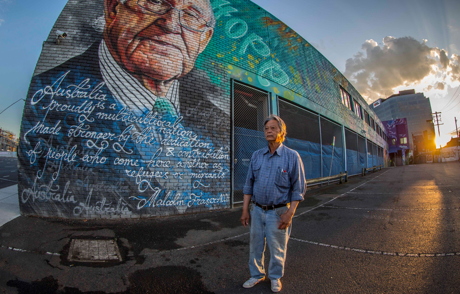 Vietnamese refugee Henry Thompson Huynh stands in front of a street art painting of Malcolm Fraser.