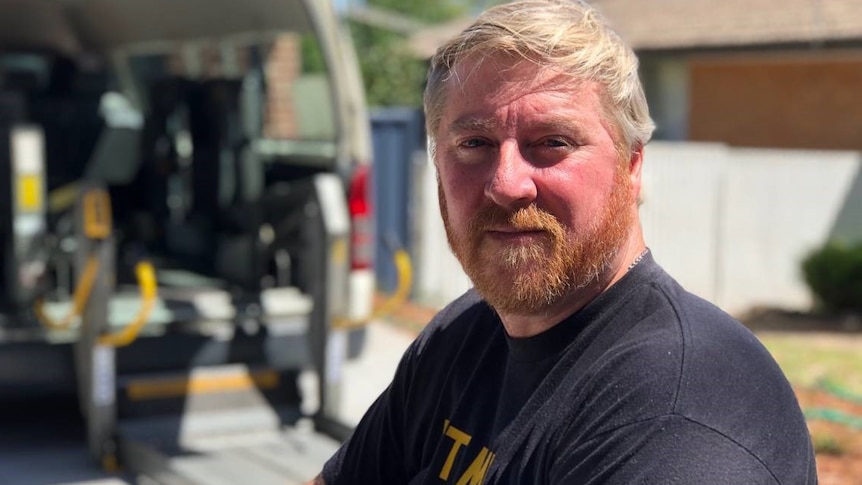 Mick Higgins looks into the camera, a disability-enabled van behind him.