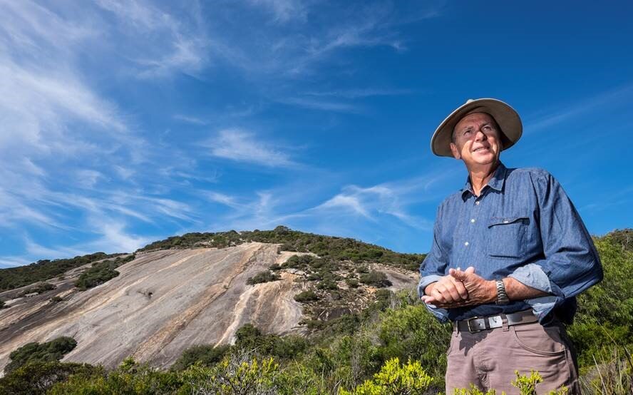 A man in a wide-brimmed hat standing in front of a granite outcrop.