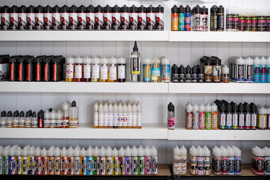 Different coloured and sized bottles of vaping liquid lined up on shelves. 