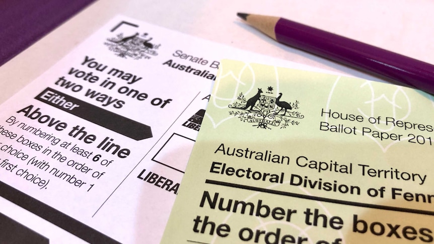 A green House or Representatives ballot paper sits on top of a white Senate ballot paper, with a purple pencil laying on top.