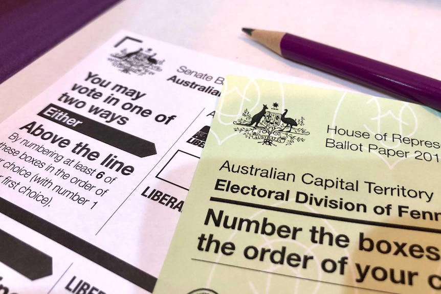 A green House or Representatives ballot paper sits on top of a white Senate ballot paper, with a purple pencil laying on top.