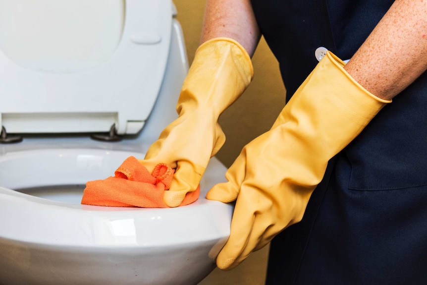 A person wearing gloves cleans a toilet, depicting the issues around cleaning in relationships.