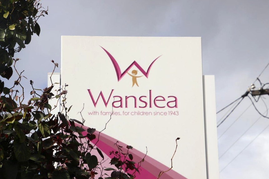 A sign advertising Wanslea family services with foliage in the foreground.