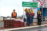 A group of people in life jackets standing on the side of the road next to food supplies