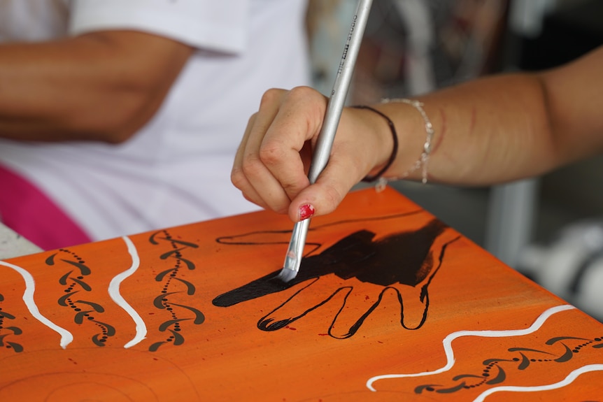 A hand holding a paintbrush, painting an Indigenous artwork