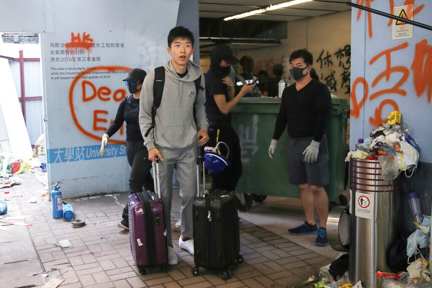一位男学生拖着行李箱，从一片混乱中走出。