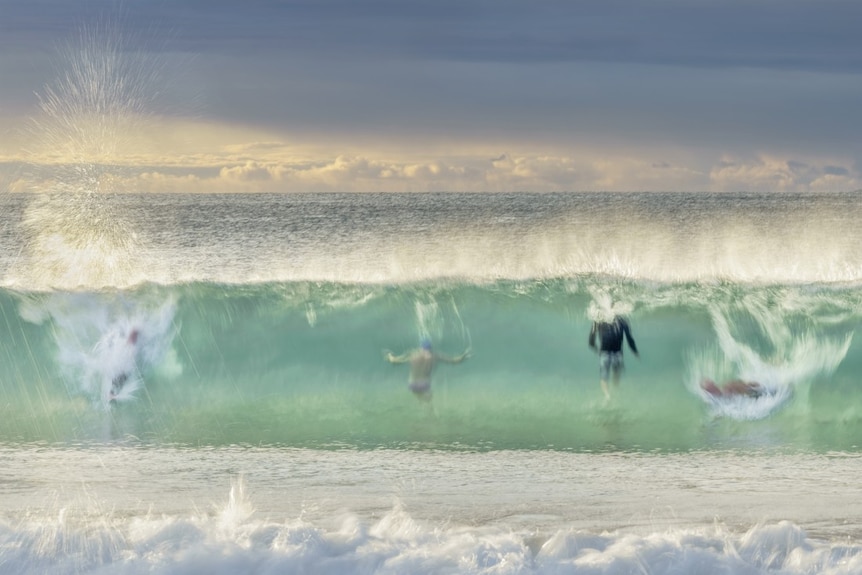 Four bodysurfers are captured inside the curl of a breaking wave in clean, bottle-green surf.