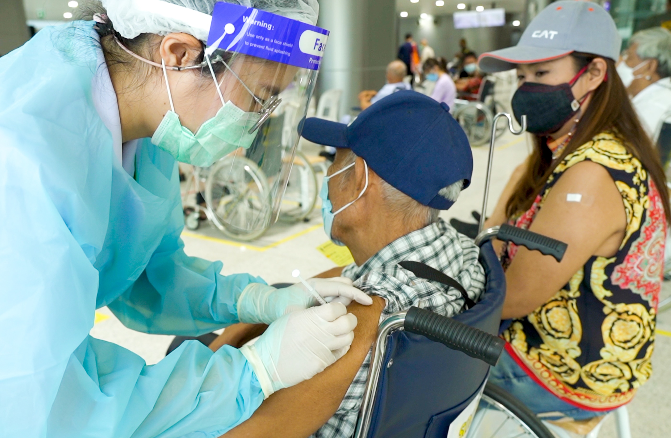 An elderly Thai man gets a needle from a nurse in his arm 
