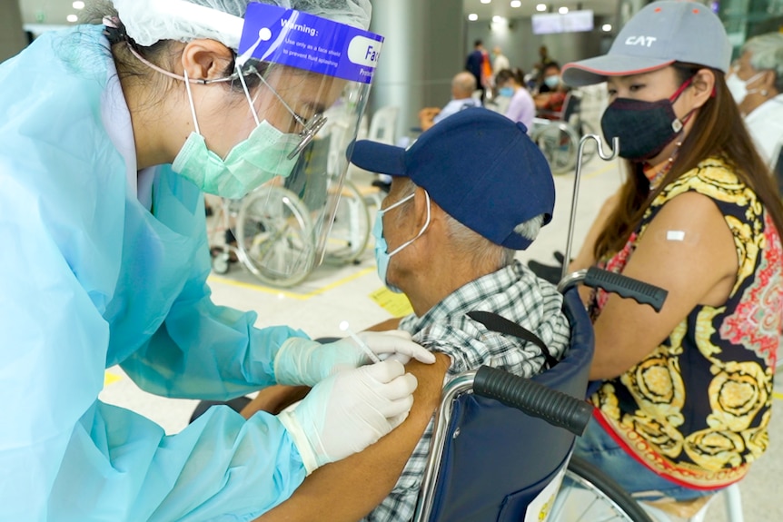 An elderly Thai man gets a needle from a nurse in his arm 