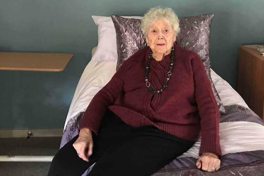 An elderly lady sits on her bed  in her nursing home.