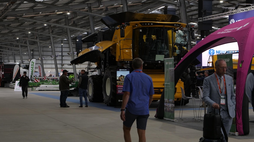 a man walks past an enormous yellow harvester inside a large shed