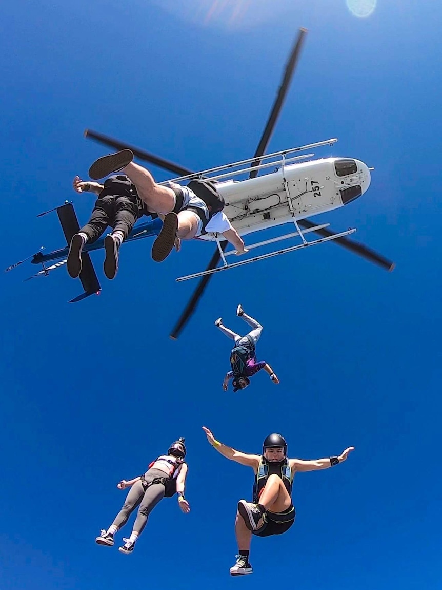People skydive out of a helicopter.