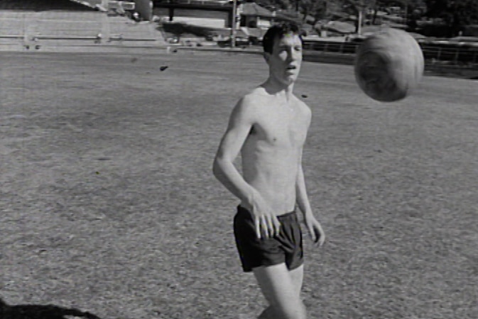 a black and white photograph of a teenage boy juggling a football with his feet