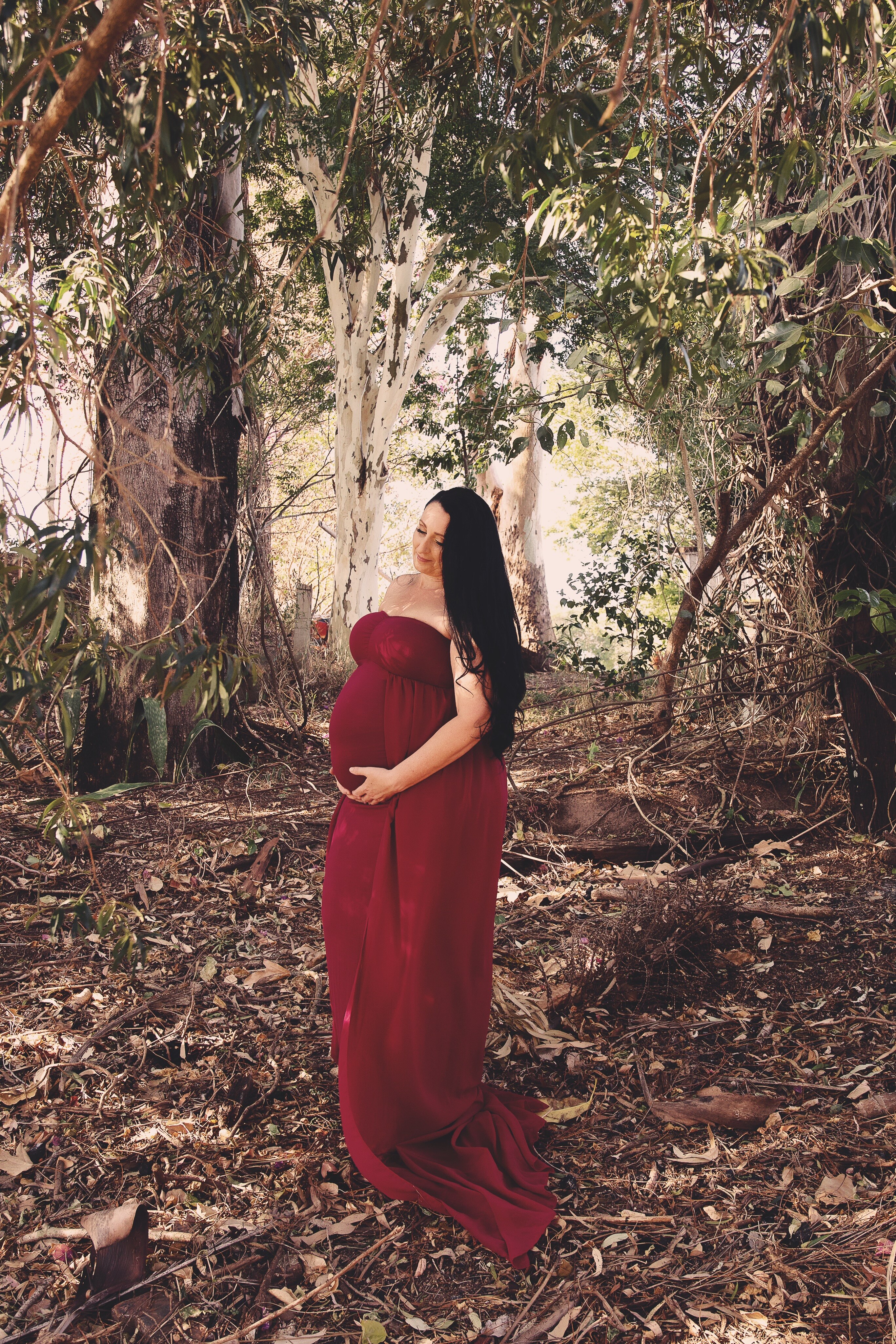 Michelle, heavily pregnant, wearing a red gown in a professional photo shoot in a forest. 