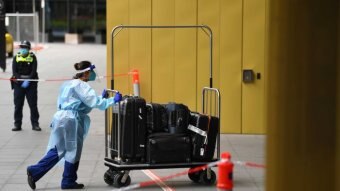 A healthcare worker in full PPE pushes luggage into a hotel.