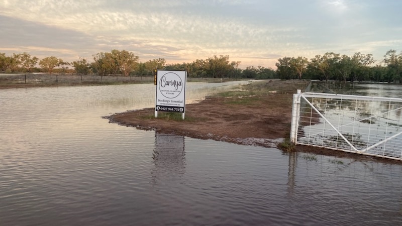 Floodwater surrounds a sign on an outback property.
