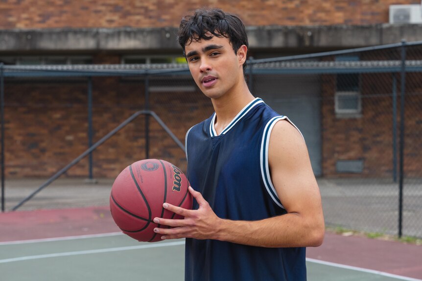 A TV still of Thomas Weatherall, a young Aboriginal man, holding a basketball and looking at the camera.