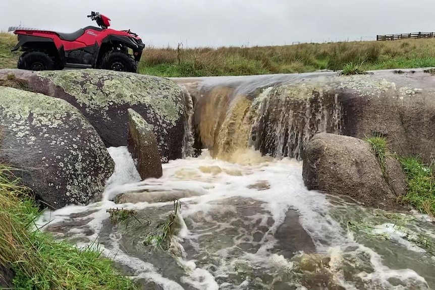 A motorbike next to a fast flowing creek.