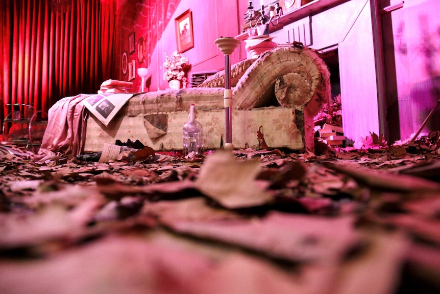 A pink room art installation which shows a sofa, a fireplace and pink leaves on the floor.