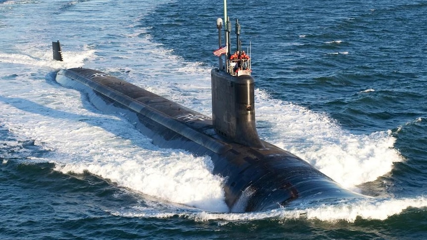 A submarine moves through the water causing a massive wake behind it, some crew visible above deck.