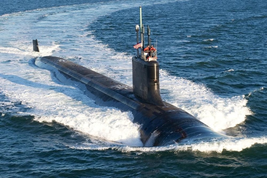 A submarine moves through the water causing a massive wake behind it, some crew visible above deck.