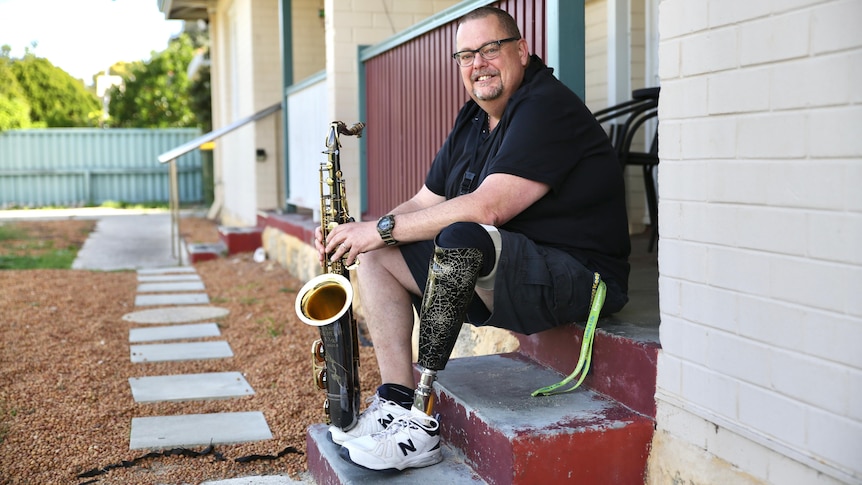 Andrew Fairbairn sitting on step playing sax.